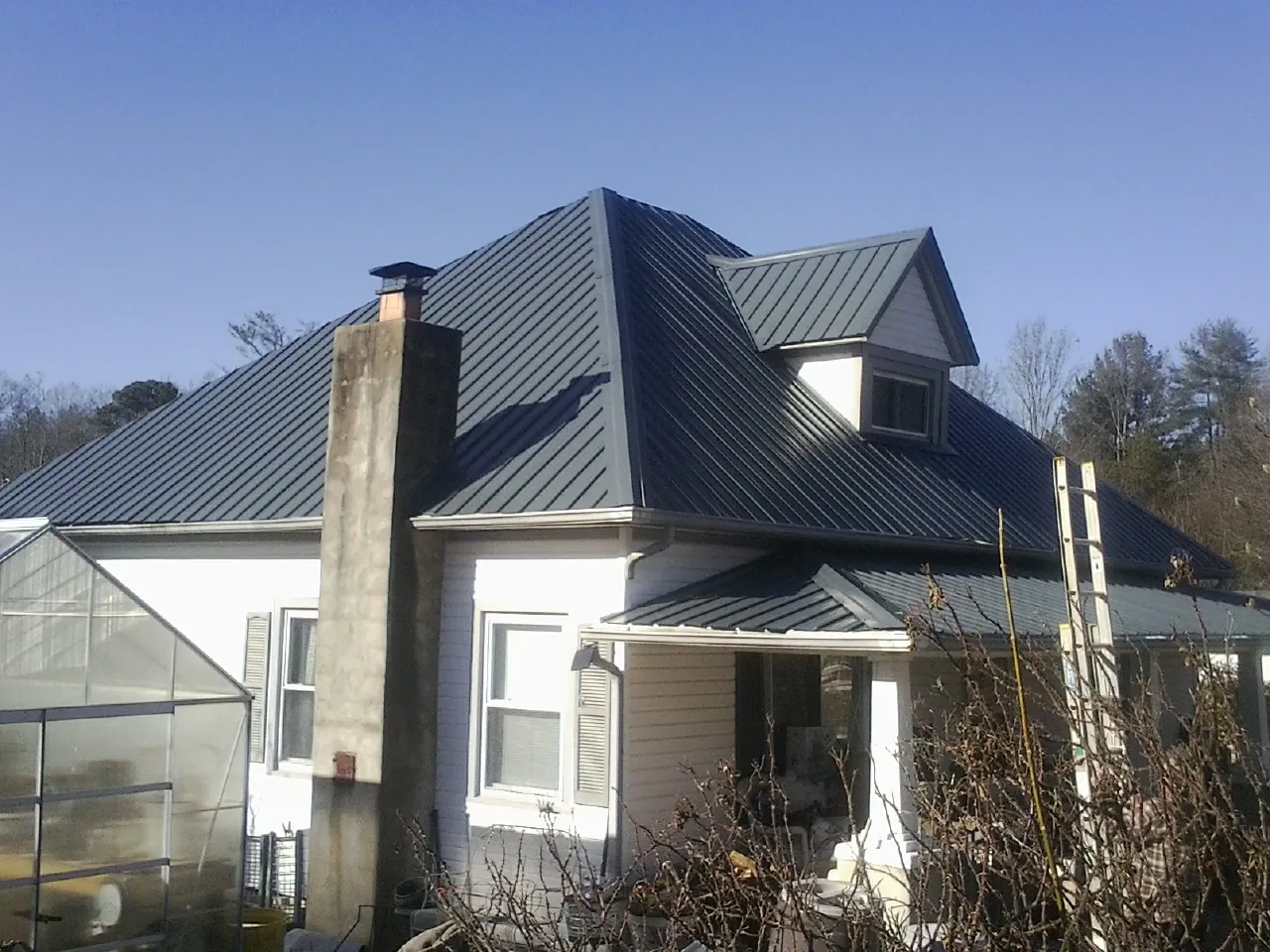 Dark blue standing seam metal roof on a white farmhouse with dormer — Slate & Tile Roof Repair by Roofing Brothers in Bouton