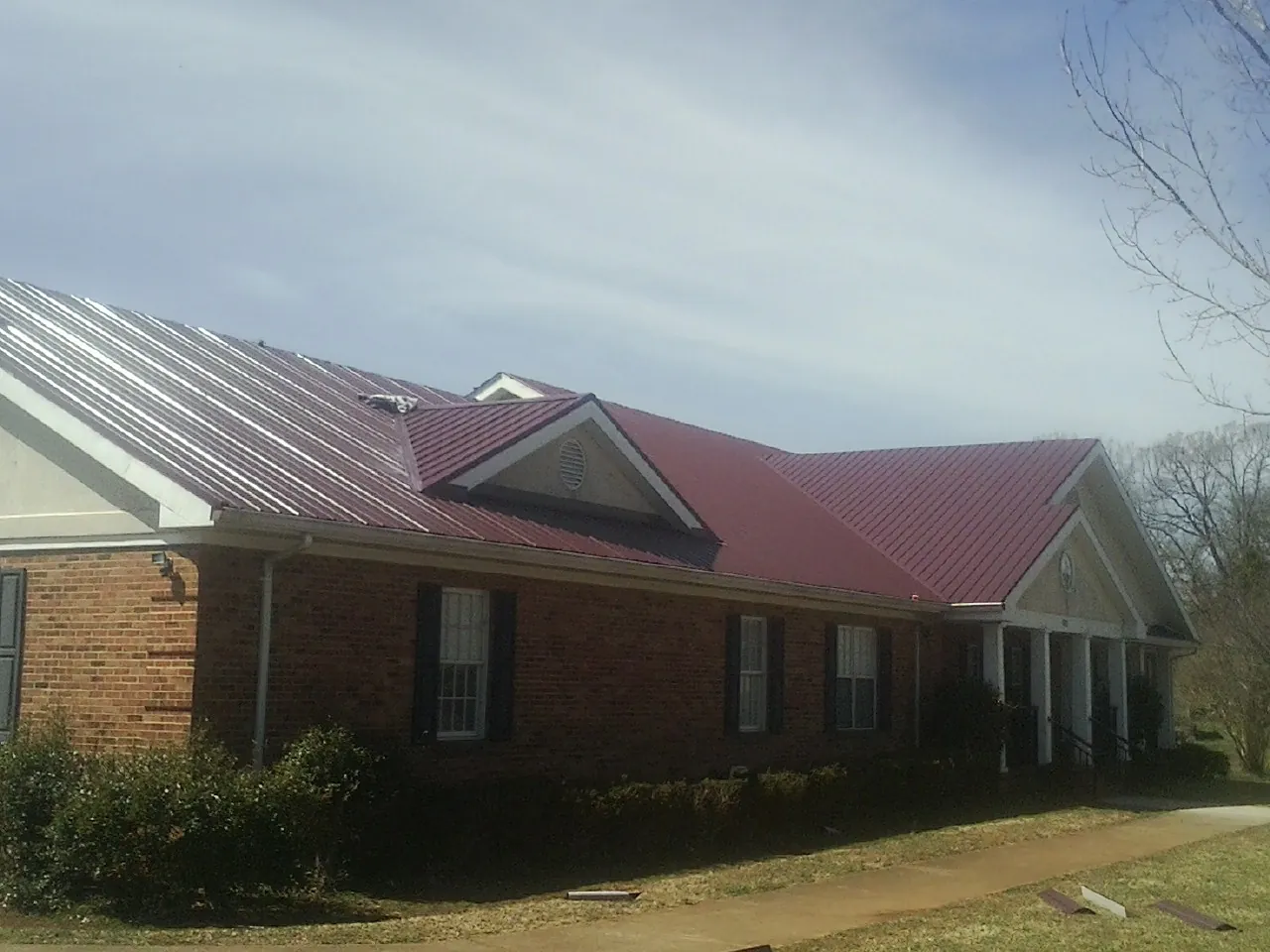 Red metal roof with gabled entries on a long brick building, from a Hail Damage Roof Repair job in Bouton