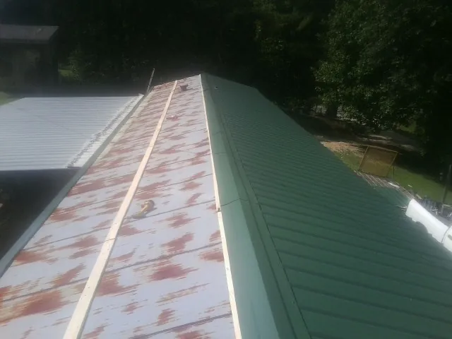 Old rusted panels beside newly installed green metal roofing — Wind Damage Roof Repair by Roofing Brothers in Bouton