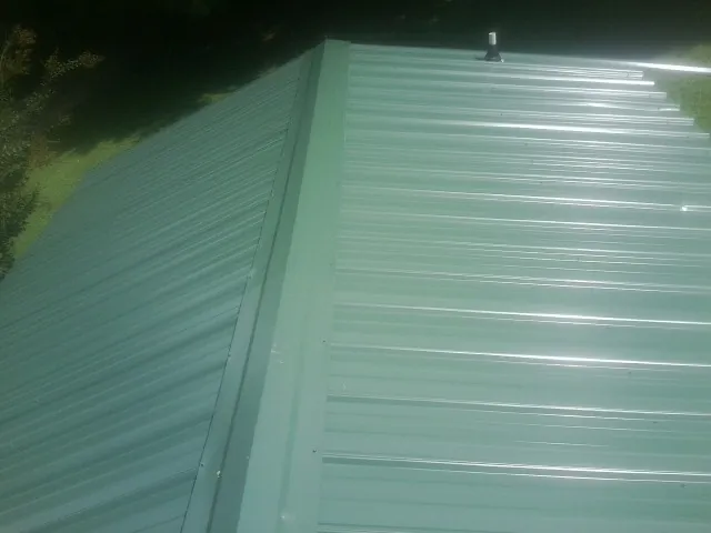 New green metal panels meeting at the ridge of a roof — Flat Roof Repair work by our crew in Bouton