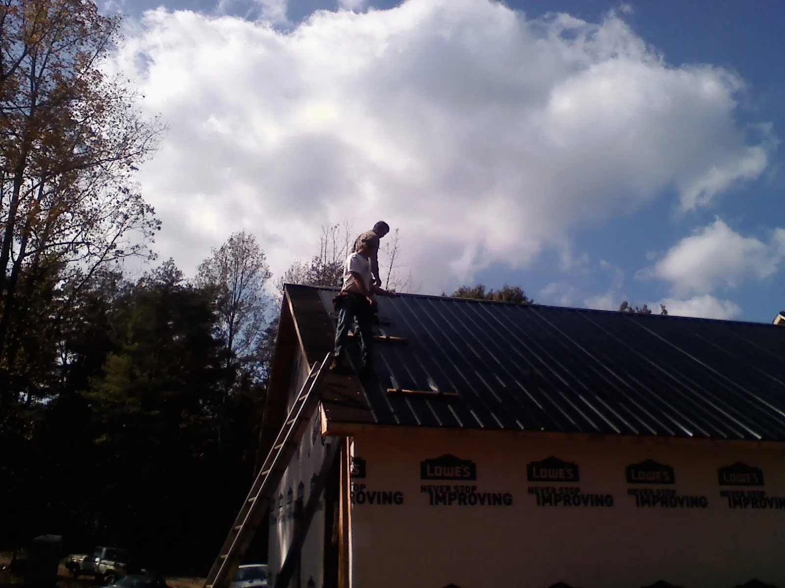 Roofer fastening dark metal panels high against a cloudy sky, from a Roof Inspection job in Bouton