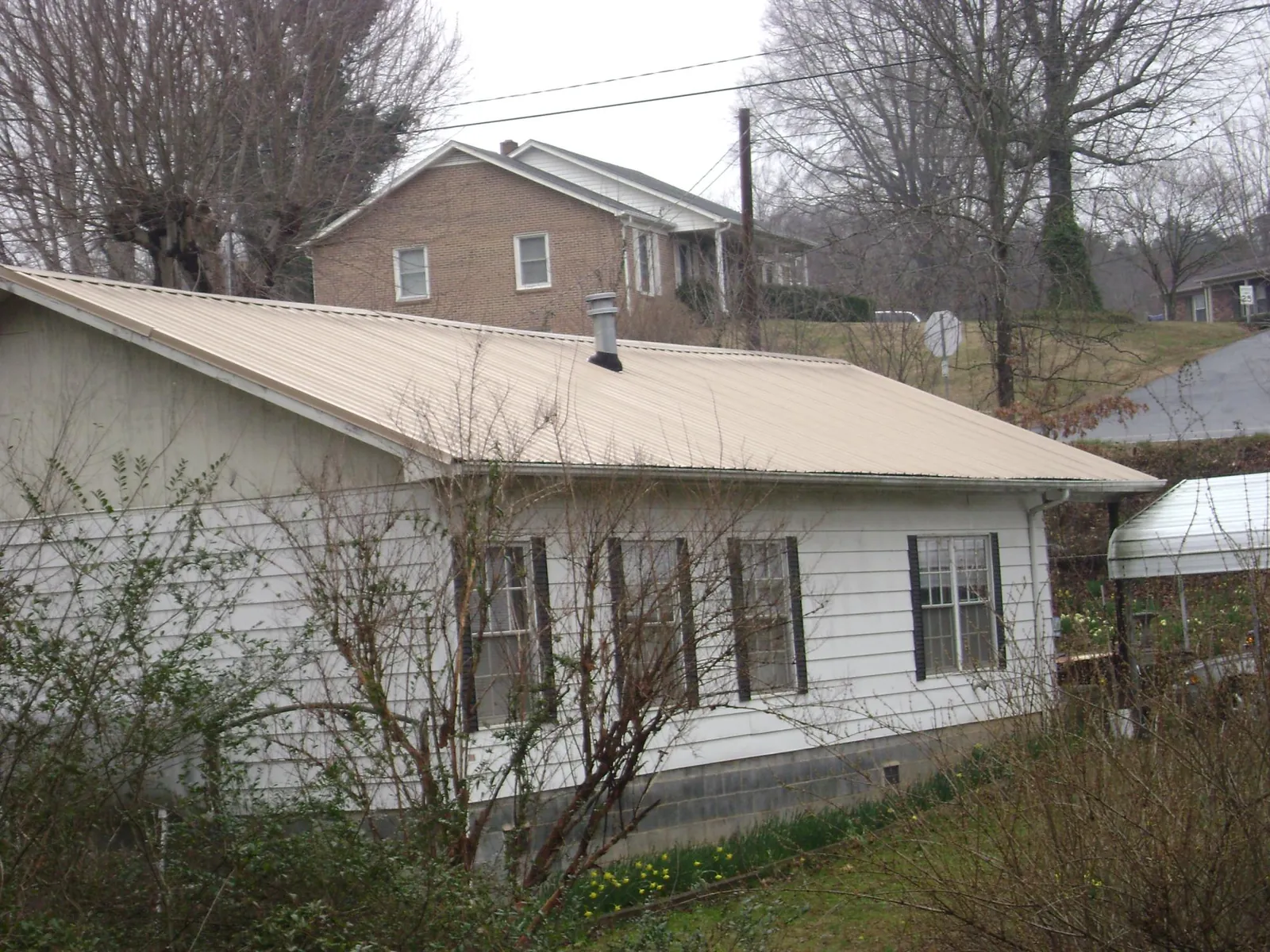 Tan metal roof on a white sided house set into a hillside — Commercial Roofing by Roofing Brothers in Bouton