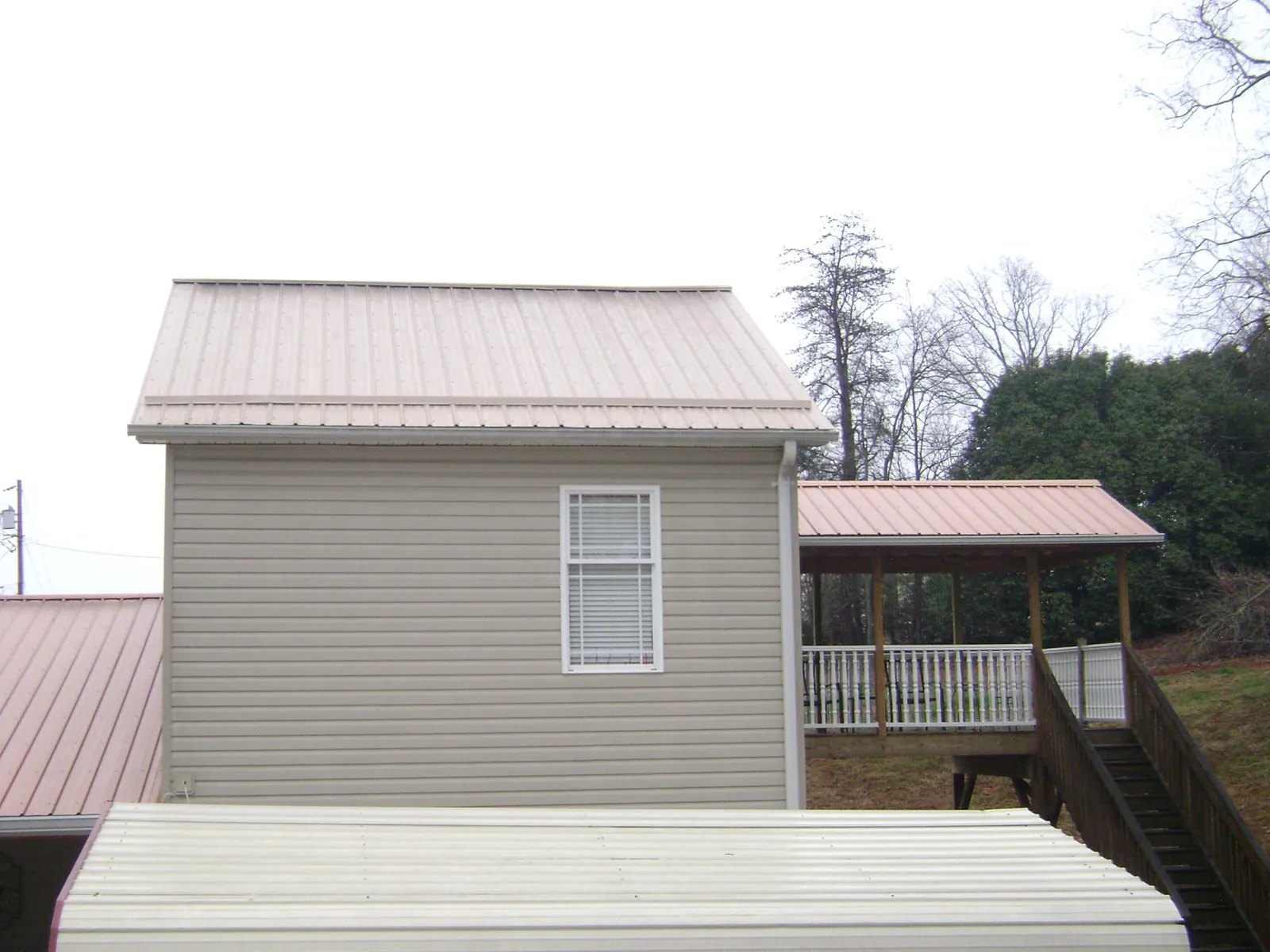Tan metal roofs on a two story addition and attached porch, from a Roof Replacement job in Bouton